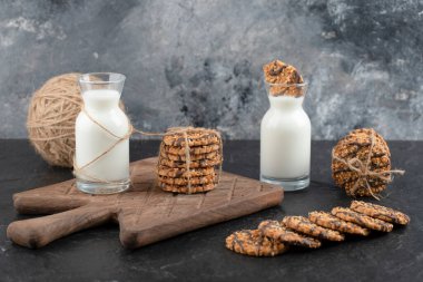 Siyah arka planda tahta kesim tahtasının üzerinde kurabiye yığını olan iki süt şişesinin yan görüntüsü. Yüksek kalite fotoğraf