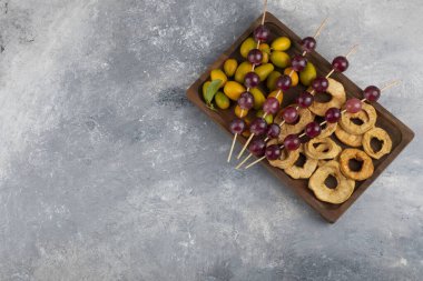 Kurumuş elma halkaları, kumkatlar ve mermer zemin üzerinde kırmızı üzümlerle dolu ahşap bir tabak. Yüksek kalite fotoğraf