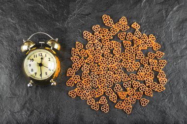 Siyah zemin üzerinde çalar saat olan çiğ makarna yığını. Yüksek kalite fotoğraf