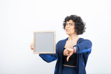 Kıvırcık saçlı, çerçeveli ve baş parmağını aşağı gösteren genç bir kadın. Yüksek kalite fotoğraf