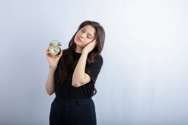 Beyaz arka planda çalar saati tutan uykulu kız görüntüsü. Yüksek kalite fotoğraf