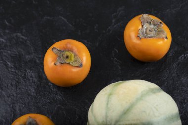 Siyah yüzeyde üç taze fuyu hurması ve kavun. Yüksek kalite fotoğraf