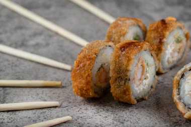 Sıcak kızarmış suşi ruloları, tek kullanımlık ahşap çubuklarla taş bir arka plana yerleştirilmiş. Yüksek kalite fotoğraf
