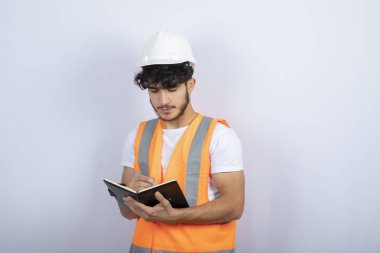 Beyaz duvarın üzerinde deftere yazılı, kasketli yakışıklı erkek mühendis. Yüksek kalite fotoğraf