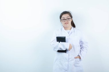 Doktor üniformalı genç bir kız ayakta ve elinde not defteri var. Yüksek kalite fotoğraf