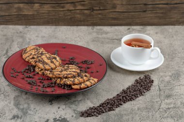 Kırmızı tabağa çikolata damlaları serpiştirilmiş lezzetli kurabiyeler ve bir fincan çay. Yüksek kalite fotoğraf