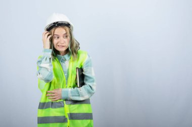 Beyaz duvarın üzerinde şakacı bir ifadeye sahip genç bayan mühendisin fotoğrafı. Yüksek kalite fotoğraf