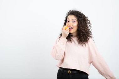 Pembe kazaklı, portakal yiyen kıvırcık kadın portresi. Yüksek kalite fotoğraf