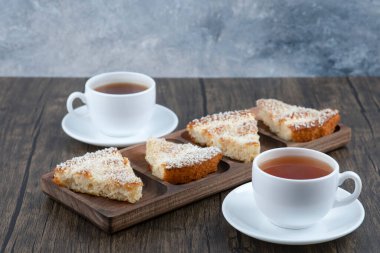 Tahta bir tahtanın üzerinde dilimlenmiş lezzetli pastayla iki fincan sıcak çay. Yüksek kalite fotoğraf