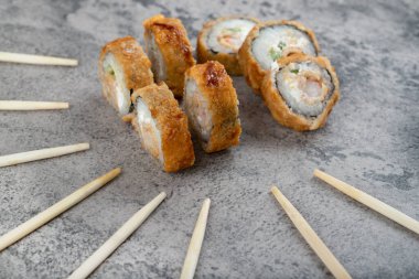 Sıcak kızarmış suşi ruloları, tek kullanımlık ahşap çubuklarla taş bir arka plana yerleştirilmiş. Yüksek kalite fotoğraf
