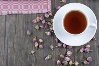 Ahşap bir masaya yerleştirilmiş gül tomurcukları olan bir fincan siyah çay. Yüksek kalite fotoğraf