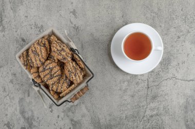 Taze pişmiş çoklu taneli kurabiyeler, sepet içinde çikolata jölesi ve bir fincan çay. Yüksek kalite fotoğraf