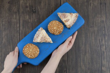 Mavi tahta, yulaf ezmeli kurabiyeler ve kek parçaları tutan kadın elleri. Yüksek kalite fotoğraf