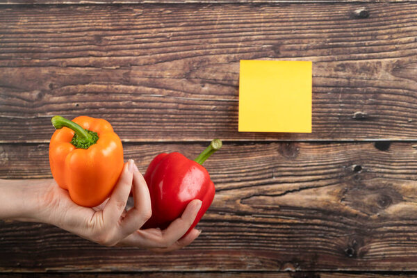 Female hands holding two ripe bell peppers on wooden background. High quality photo