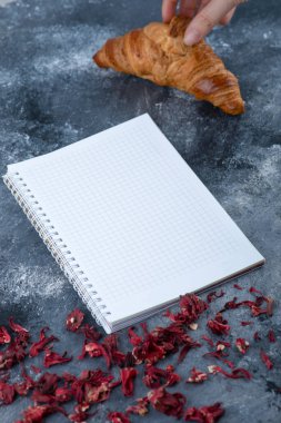 Dişi el, defterin yanında taze ve lezzetli bir kruvasan alıyor. Yüksek kalite fotoğraf