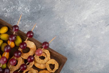 Kurumuş elma halkaları, kumkatlar ve mermer zemin üzerinde kırmızı üzümlerle dolu ahşap bir tabak. Yüksek kalite fotoğraf