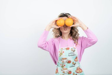 Önlüklü genç kıvırcık kadın portresi gözlerinin önünde portakal tutuyor. Yüksek kalite fotoğraf