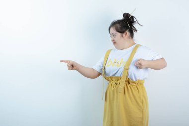 Genç ve güzel bir kız model, beyaz duvarda durup, parmaklarıyla işaret ediyor. Yüksek kalite fotoğraf