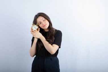 Beyaz arka planda uyuyan çalar saati olan genç bir kız resmi. Yüksek kalite fotoğraf