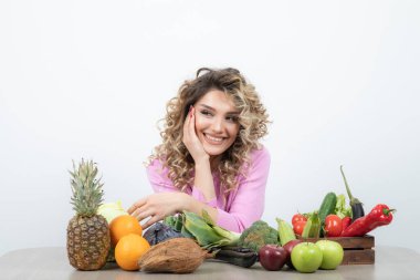 Masada bir sürü meyveyle oturan pembe elbiseli sarışın kadının fotoğrafı. Yüksek kalite fotoğraf
