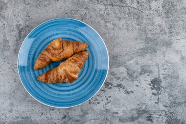 Taş yüzeyde mavi bir tabak taze çikolatalı kruvasan. Yüksek kalite fotoğraf