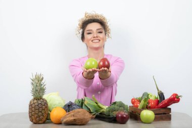 Kıvırcık kadın bir sürü taze sebzeyle masada oturuyor.