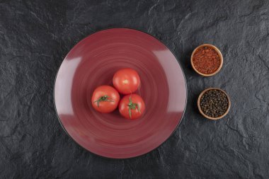 Siyah zemin üzerinde biber ve biber tozu olan üç taze kırmızı domates tabağı. Yüksek kalite fotoğraf