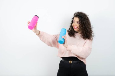 Pembe ve mavi su şişeleri tutan kazaklı genç kıvırcık kadın. Yüksek kalite fotoğraf