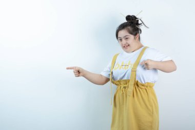 Genç ve güzel bir kız model, beyaz duvarda durup, parmaklarıyla işaret ediyor. Yüksek kalite fotoğraf