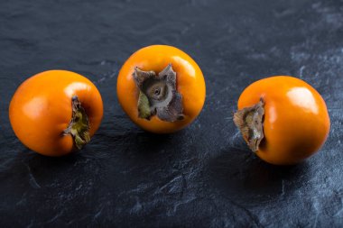 Siyah yüzeye yerleştirilmiş üç taze fuyu hurması. Yüksek kalite fotoğraf