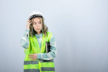 Beyaz duvarın üzerinde şakacı bir ifadeye sahip genç bayan mühendisin fotoğrafı. Yüksek kalite fotoğraf