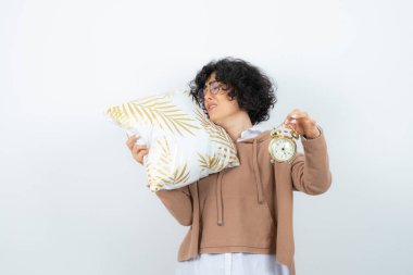 Beyaz arka planda yastıkla poz veren genç bir kadın.