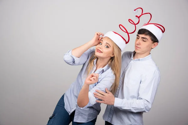 灰色の背景にサンタの帽子に立つ素敵な若いカップル 高品質の写真 — ストック写真