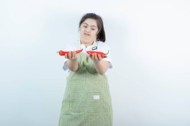 Kareli önlüğün içinde duran ve elinde iki kırmızı acı biber tutan genç ve güzel bir kız. Yüksek kalite fotoğraf