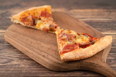 Tahta kesme tahtasının üzerinde pepperonili iki dilim lezzetli pizza. Yüksek kalite fotoğraf