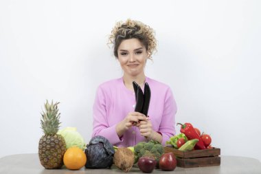 Meyve ve sebzelerle masada otururken elinde patlıcan tutan genç bir kadın. Yüksek kalite fotoğraf