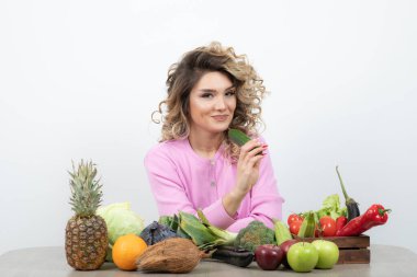 Kıvırcık kadın bir sürü taze sebzeyle masada oturuyor.