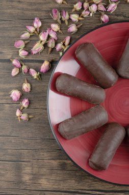 Çikolatalı kremayla dolu kırmızı bir tabak süt kremalı ve ahşap bir masada kurumuş güller. Yüksek kalite fotoğraf