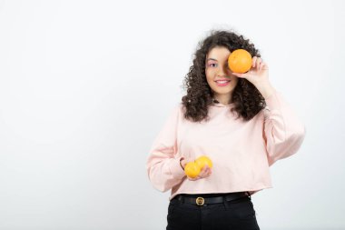 Pembe kazaklı genç kıvırcık kadın gözünün önünde portakal tutuyor. Yüksek kalite fotoğraf