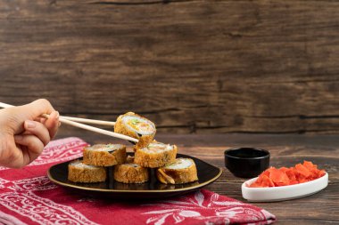 Dişi el, ahşap yüzeyinde çubuklarla sıcak suşi rulosu alıyor. Yüksek kalite fotoğraf