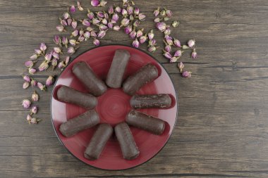 Çikolatalı kremayla dolu kırmızı bir tabak süt kremalı ve ahşap bir masada kurumuş güller. Yüksek kalite fotoğraf