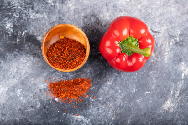 Red bell pepper and wooden bowl of ground chili on marble. High quality photo