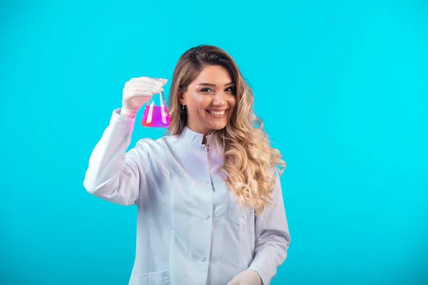 ピンクの液体で化学フラスコを保持し 肯定的な感じ白い制服の看護師 高品質の写真 — ストック写真