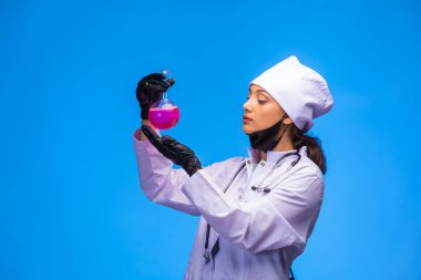 El ve yüz maskesi takan izole hemşire kimyasal şişeyi tutuyor ve dikkatli bakıyor. Yüksek kalite fotoğraf