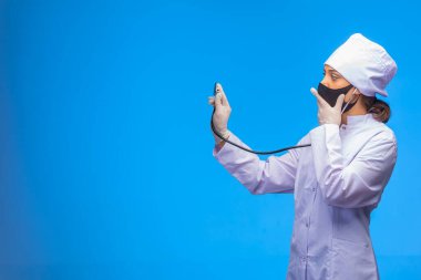 Siyah maskeli genç hemşire ağzını kapatırken hastayı steteskopla kontrol ediyor. Yüksek kalite fotoğraf