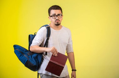 Gözlüklü, sırt çantalı ve kitabı yorgun görünen bir adam. Yüksek kalite fotoğraf