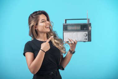 Siyah gömlekli genç bir kız elinde klasik bir radyo tutuyor ve onu işaret ediyor. Yüksek kalite fotoğraf