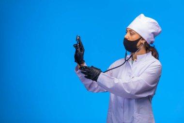 Tecrit edilmiş hemşire elinde steteskopla ve yüzünde maskeyle hastayı kontrol ediyor. Yüksek kalite fotoğraf