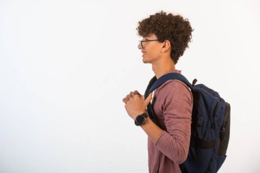 İdeal gözlüklü kıvırcık saçlı çocuk sırt çantasını sola doğru tutuyor. Yüksek kalite fotoğraf