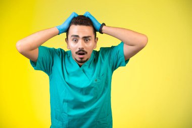 Yeşil üniformalı ve el maskeli doktor sarı arka planda hayal kırıklığına uğramış ve kafası karışmış. Yüksek kalite fotoğraf